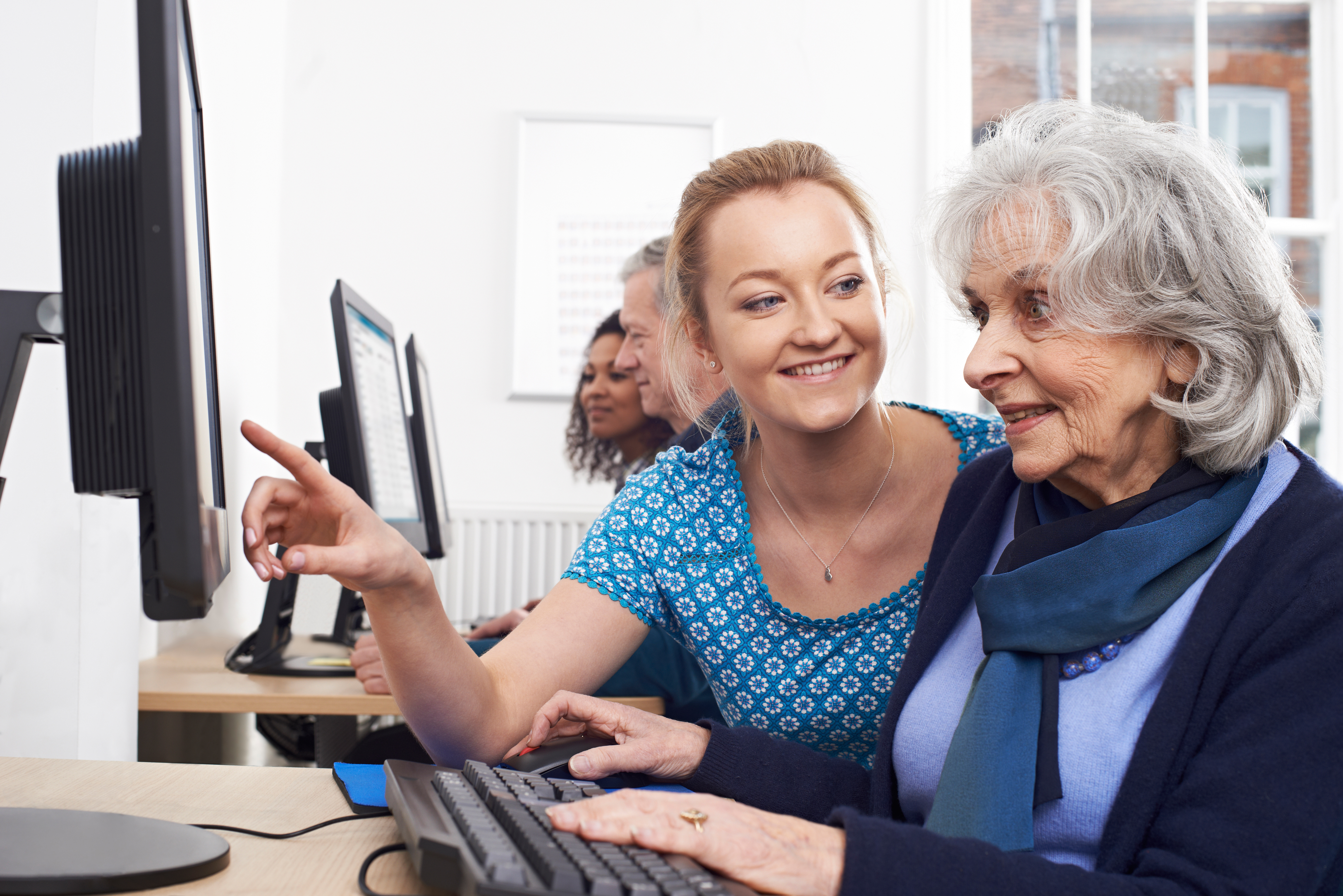 Younger women helping older woman on desktop computer