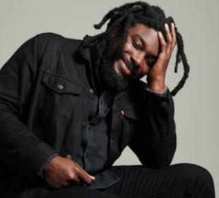Jason Reynolds in black button up, smiling resting his head on his hand