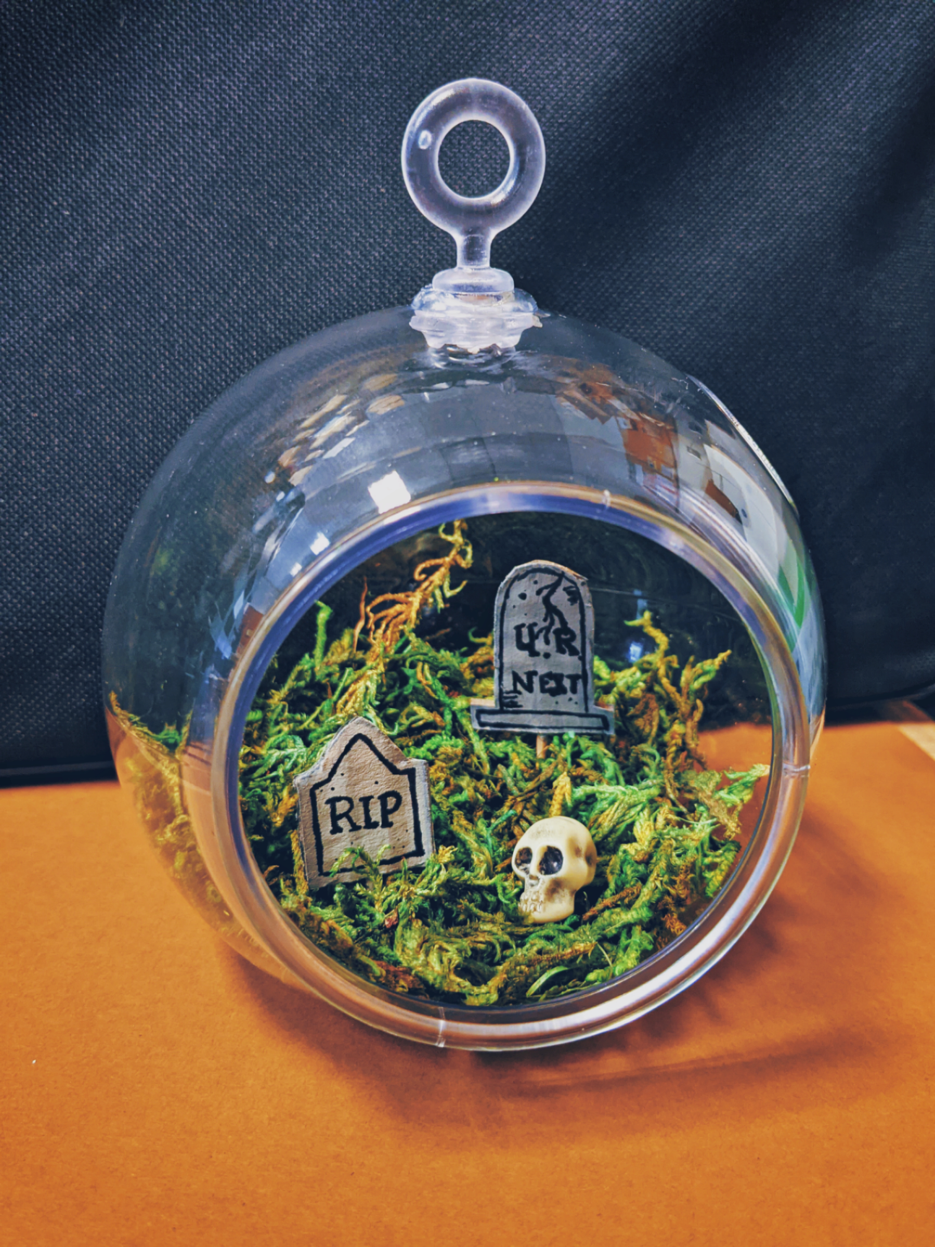 terrarium with green moss, two headstones, and skull inside