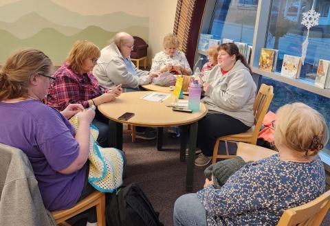 YarnTales group meeting in the library.  Several ladies gathered around tables near the front window